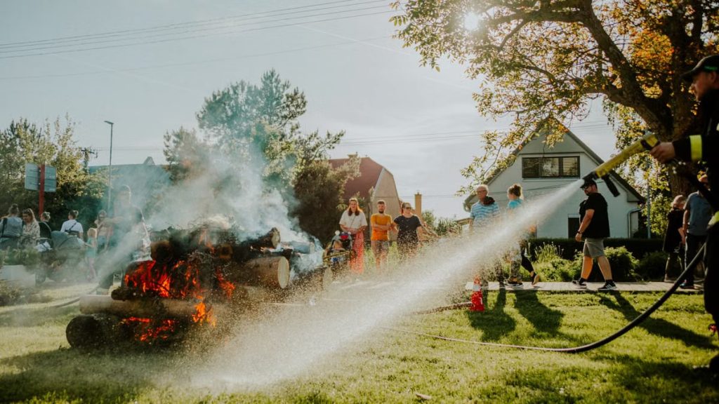 Firefighter showcases safety techniques on a controlled fire at a community event in the park.